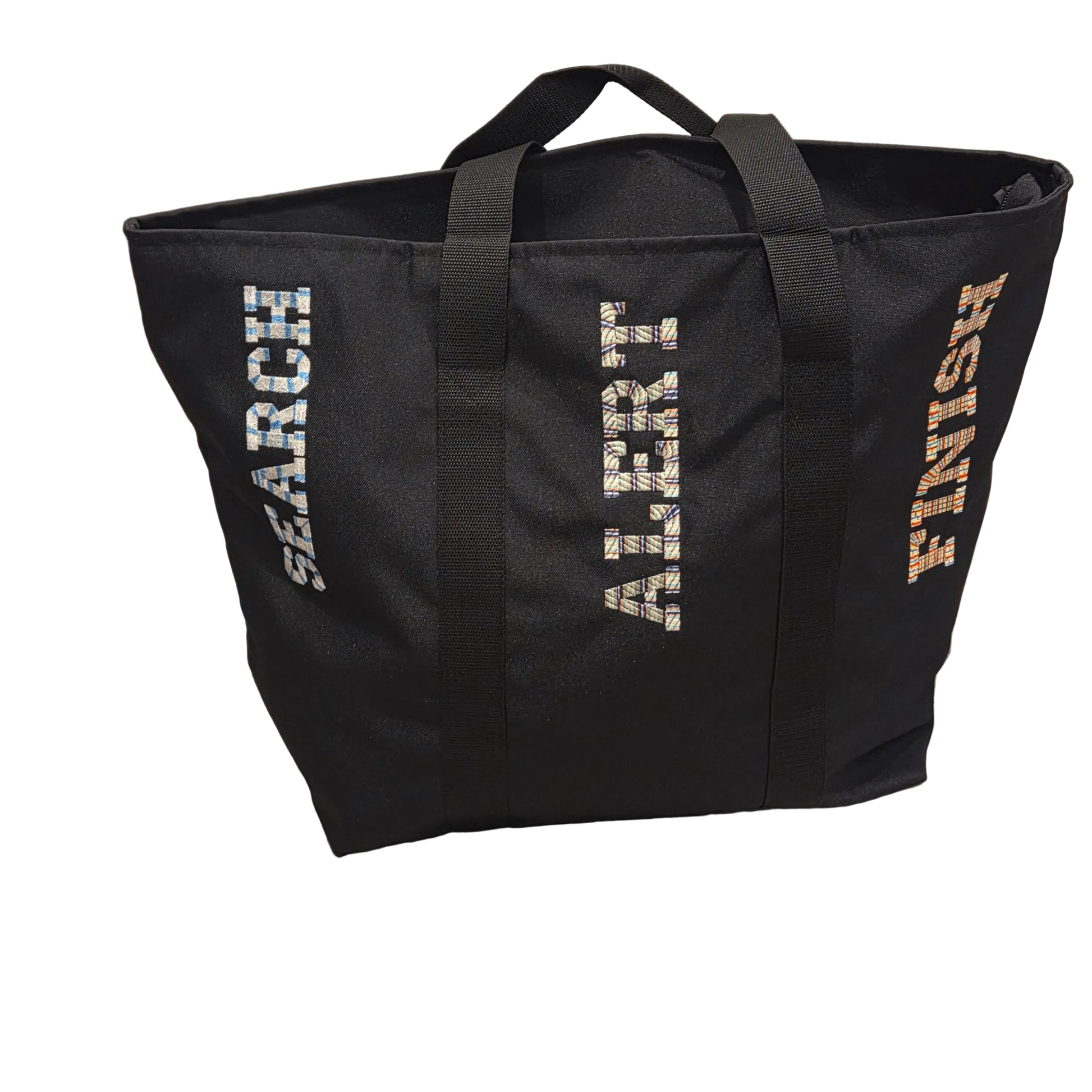 A black canvas tote bag with the words 'SEARCH', 'ALERT', and 'FINISH' printed vertically in white, glittery silver, and orange text, placed on a light wood floor against a white wall.