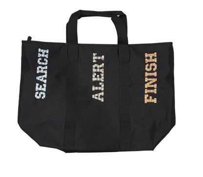 A black canvas tote bag laid flat on a light gray wood floor, featuring the words 'SEARCH', 'ALERT', and 'FINISH' printed vertically in white, silver, and gold respectively on the front.